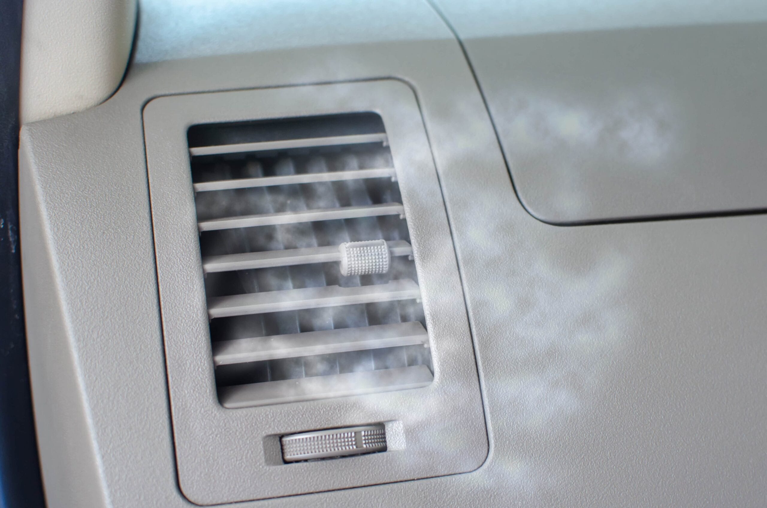 White smoke or vapor blowing out of a car dashboard air conditioning vent, suggesting an AC system failure or mechanical issue.