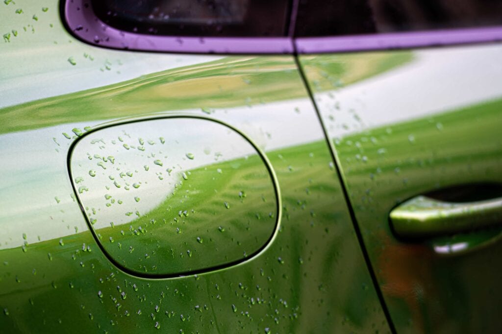 A close-up shot of a lime green luxury car's fuel door and side panel showing tight water beading droplets after rain, demonstrating a high-quality ceramic coating or wax protection.