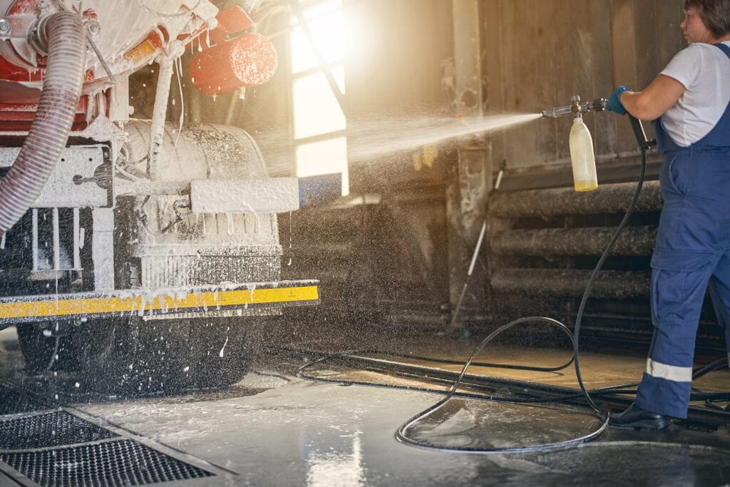 A professional technician using a high-pressure foam cannon to perform industrial fleet pressure washing on a large commercial truck in Florida.
