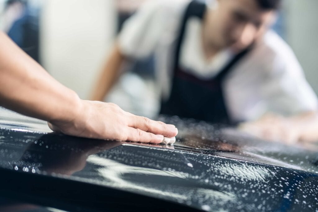 A professional detailer performing a clay bar treatment to remove surface contaminants from a black vehicle's paint during an auto detailing service in Florida.